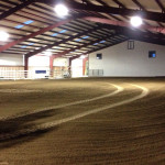 Interior of indoor riding arena with steel framing and dirt floor