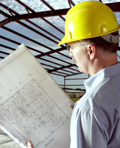 Image of a man in a hard hat reading plans with steel framing in the background.