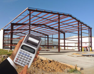 A man's hands clutching a calculator near a steel frame as he calculates the metal building cost.