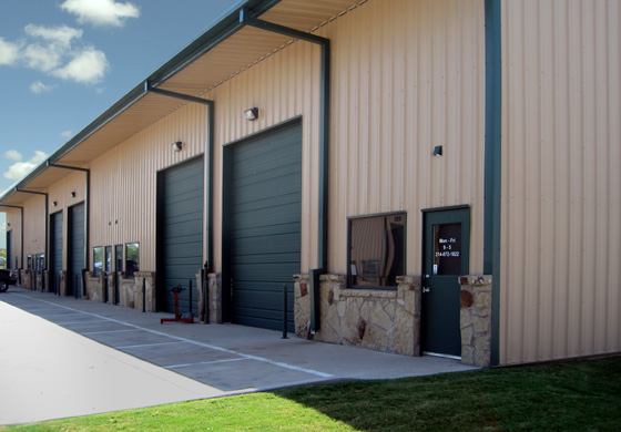 An attractive tan and green industrial metal building with large bay doors and rock trim
