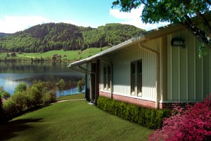 Residential metal building sits on a grassy slope above a hill-lined lake