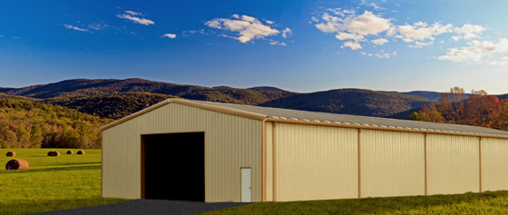 Long agricultural metal building with gold trim against a background of rolling, tree-covered hills and hay pastures