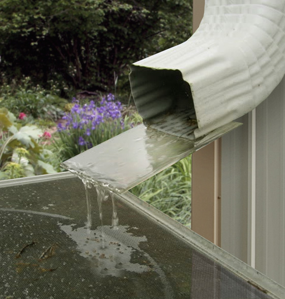 A large steel gutter on a metal building pours rain into a barrel