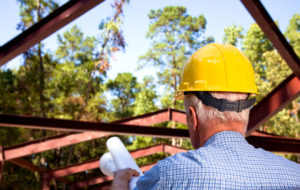 Photo of a man in a hard hat supervising the placement of a steel building rafter.