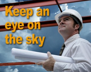 Man in hard hat carrying building plans keeps an eye on the sky to avoid dangerous lightning on a construction site 