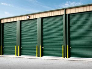 Photo of a tan self storage building with deep green roll-up doors.