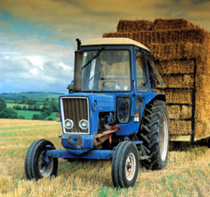 Photo of a blue tractor pulling a trailer of hay bales from the field.