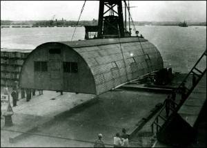 Historical photograph of early Quonset hut being carried by a crane