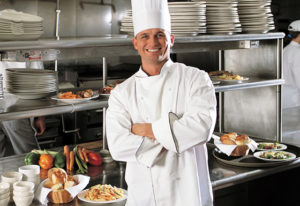 Photo of smiling chef in busy restaurant kitchen.