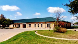 Photo of a brick commercial building with a green hip roof, built with a RHINO pre-engineered metal building.