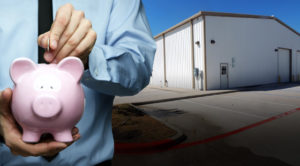Photo of a man putting money in a piggy bank as he stands before his new metal building.