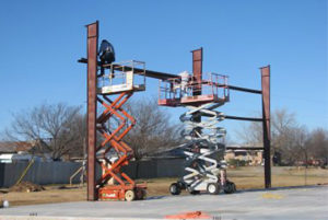 photo showing erectors using scissor lifts to assemble a steel building kit.