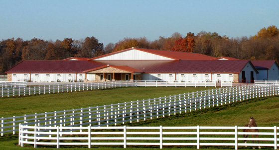 Photo of a gorgeous RHINO horse stables with a red metal roof.