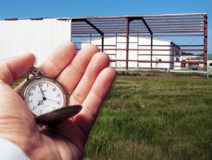 Steel building under construction with hand holding stopwatch in foreground.